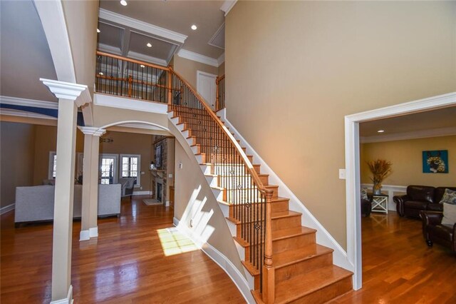 staircase with a fireplace, wood finished floors, a towering ceiling, ornamental molding, and decorative columns