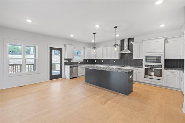 kitchen featuring stainless steel appliances, wall chimney exhaust hood, a kitchen island, recessed lighting, and tasteful backsplash