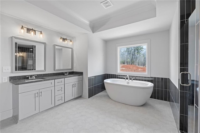full bathroom featuring a wainscoted wall, a soaking tub, double vanity, tile walls, and tile patterned floors