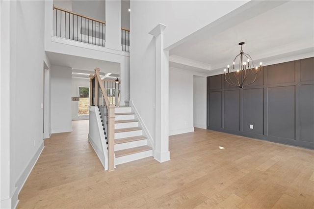 foyer with stairs, a chandelier, crown molding, light wood finished floors, and a decorative wall