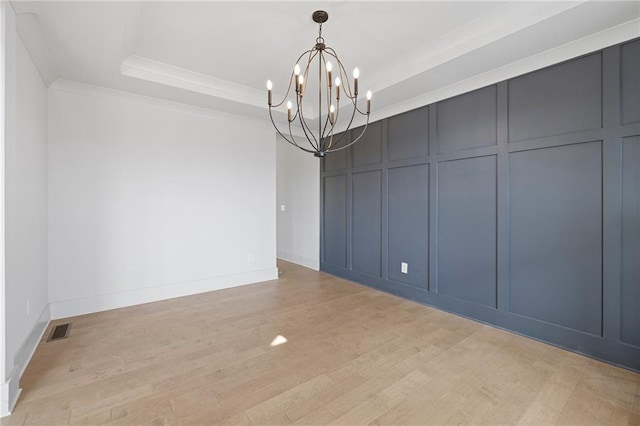 unfurnished dining area with a decorative wall, a chandelier, ornamental molding, light wood-type flooring, and a tray ceiling