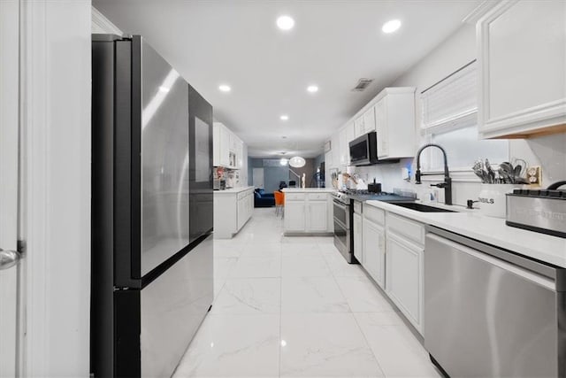 kitchen with a sink, stainless steel appliances, light countertops, white cabinets, and marble finish floor