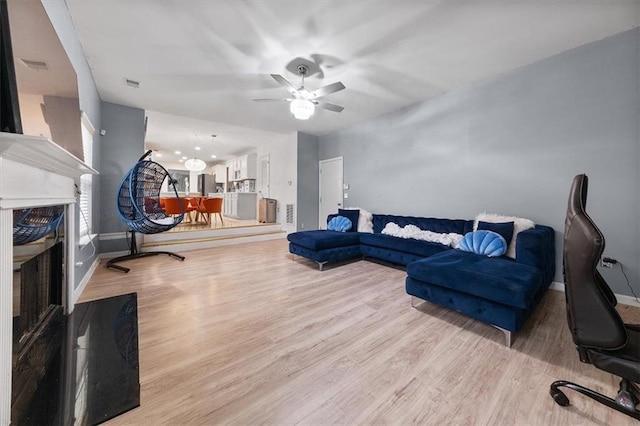 living area with a ceiling fan, wood finished floors, visible vents, baseboards, and a fireplace