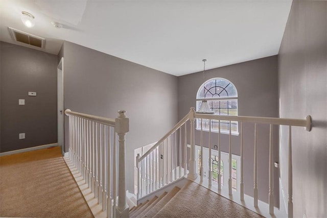 hallway with visible vents, baseboards, carpet floors, an upstairs landing, and a towering ceiling