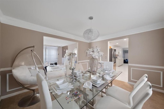 dining area featuring light carpet, ornamental molding, wainscoting, and a decorative wall