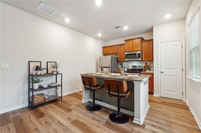 kitchen with light stone countertops, appliances with stainless steel finishes, a breakfast bar, a kitchen island with sink, and light hardwood / wood-style flooring