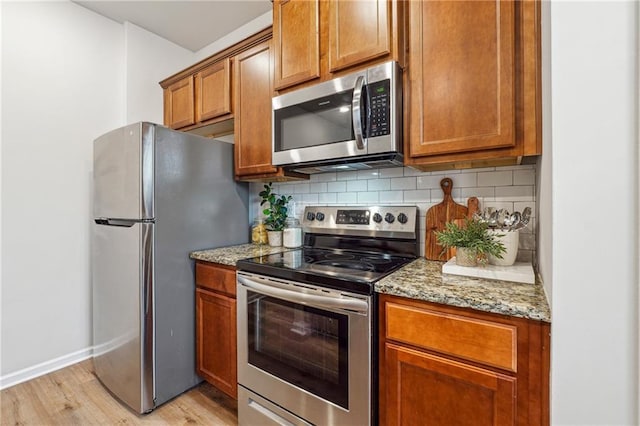 kitchen with light stone countertops, appliances with stainless steel finishes, light hardwood / wood-style floors, and tasteful backsplash