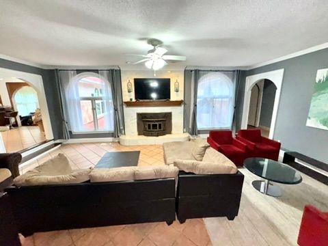 living room with ceiling fan, crown molding, light tile patterned floors, and a textured ceiling