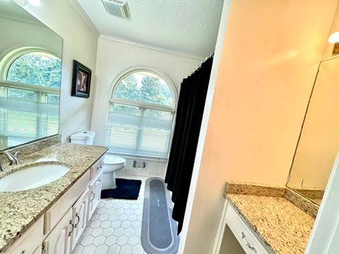 bathroom with toilet, crown molding, a textured ceiling, vanity, and tile patterned flooring