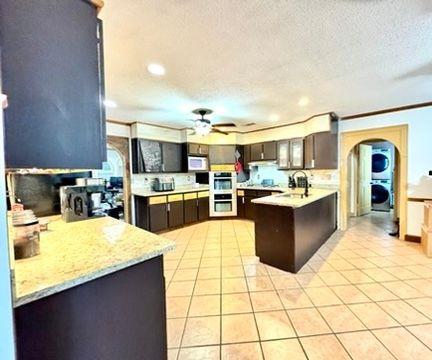 kitchen with stacked washer and clothes dryer, ceiling fan, kitchen peninsula, dark brown cabinets, and a textured ceiling