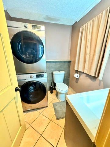 bathroom featuring stacked washer / dryer, vanity, toilet, tile patterned floors, and a textured ceiling