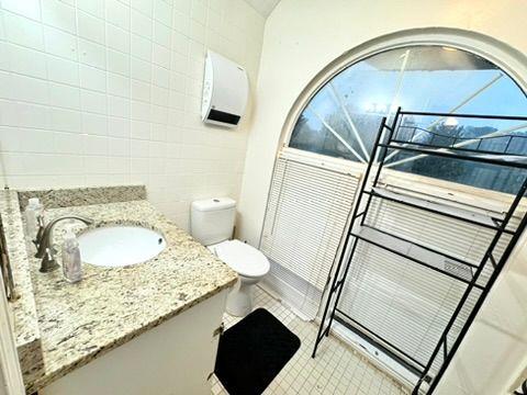 bathroom with tile walls, vanity, tile patterned flooring, and toilet