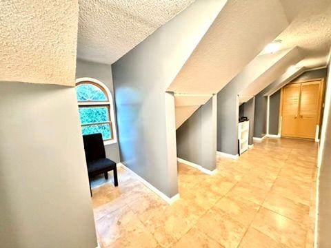 hall with lofted ceiling, tile patterned floors, and a textured ceiling