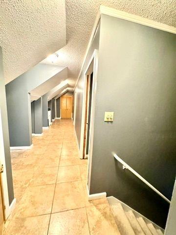 corridor featuring light tile patterned floors, vaulted ceiling, and a textured ceiling