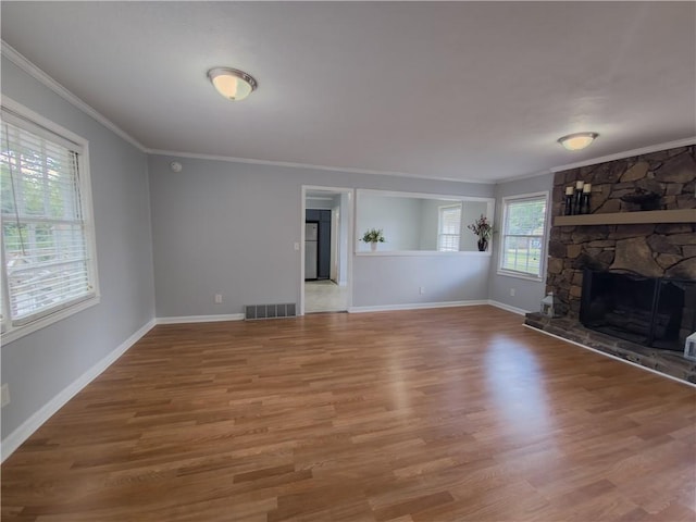 unfurnished living room with wood-type flooring, ornamental molding, and a stone fireplace