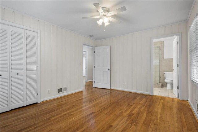 unfurnished bedroom featuring a closet, connected bathroom, light hardwood / wood-style floors, and ceiling fan