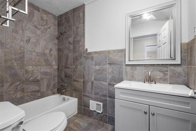 full bathroom featuring vanity, tiled shower / bath combo, toilet, a textured ceiling, and tile walls