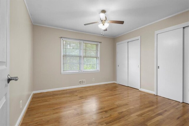 unfurnished bedroom featuring ceiling fan, two closets, ornamental molding, and light hardwood / wood-style flooring