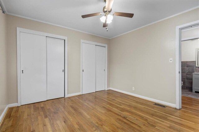 unfurnished bedroom with light wood-type flooring, two closets, ceiling fan, and ornamental molding