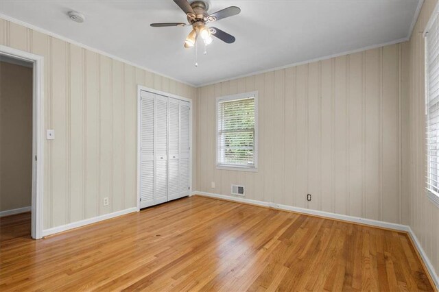 unfurnished bedroom featuring ceiling fan, light wood-type flooring, ornamental molding, and a closet