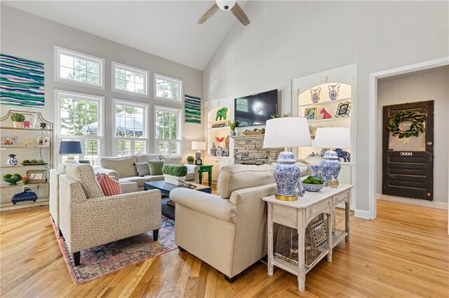 living room with baseboards, built in features, light wood-style flooring, ceiling fan, and high vaulted ceiling
