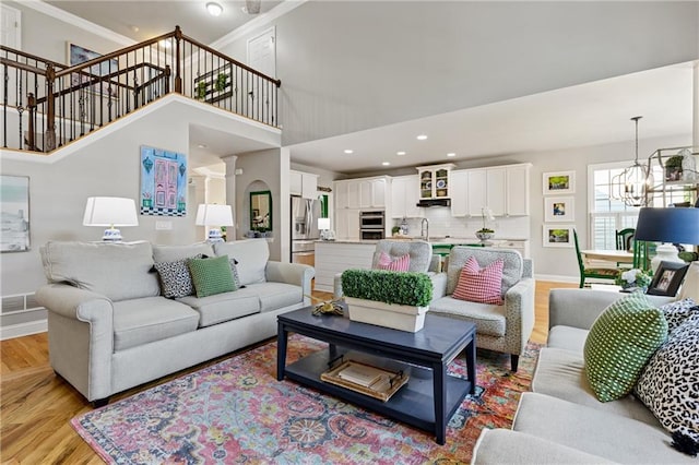 living room with a notable chandelier, baseboards, ornamental molding, light wood-style flooring, and visible vents