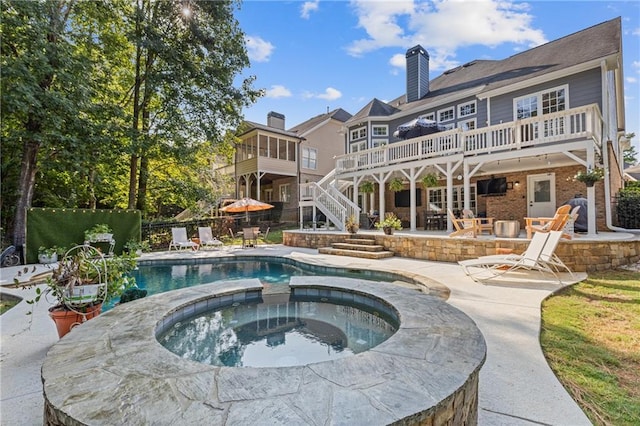 back of house with a patio, a chimney, an in ground hot tub, stairs, and a wooden deck