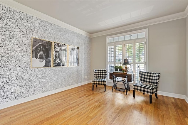 sitting room featuring baseboards, wallpapered walls, crown molding, an accent wall, and wood finished floors