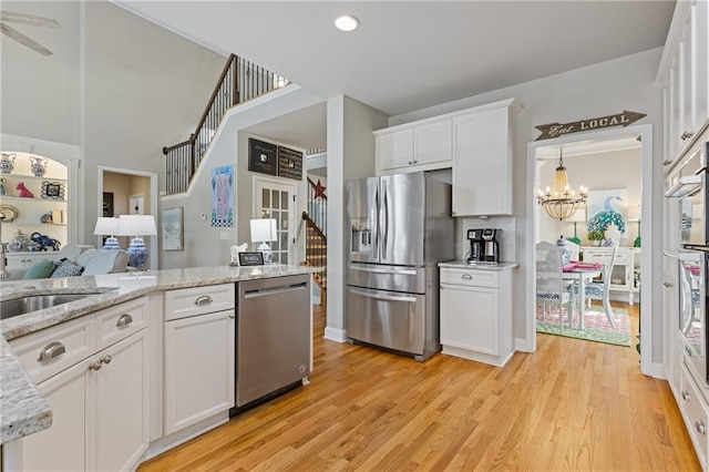 kitchen featuring an inviting chandelier, light wood-style flooring, white cabinetry, a sink, and stainless steel appliances