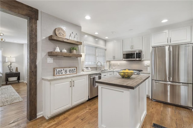 kitchen featuring butcher block countertops, white cabinets, stainless steel appliances, light wood finished floors, and a sink