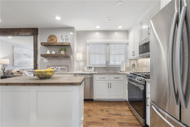 kitchen with light wood-style flooring, tasteful backsplash, white cabinets, a sink, and stainless steel appliances