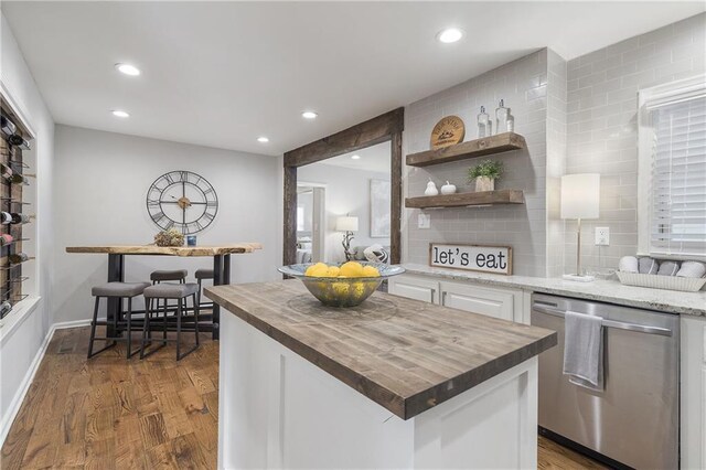 kitchen with stainless steel dishwasher, white cabinetry, wood finished floors, wooden counters, and backsplash