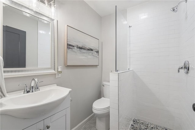 full bath with toilet, vanity, baseboards, and a tile shower