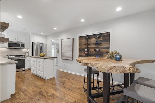 kitchen featuring tasteful backsplash, a center island, light wood-style floors, white cabinetry, and stainless steel appliances