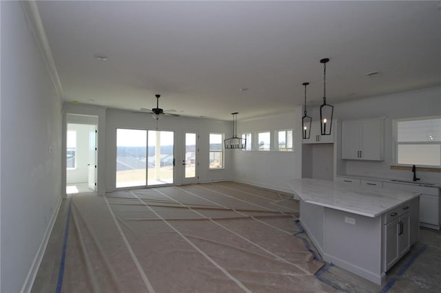 kitchen featuring a sink, a ceiling fan, baseboards, white cabinets, and a center island