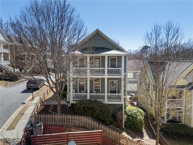 neoclassical / greek revival house featuring a fenced front yard, a porch, a standing seam roof, metal roof, and a balcony