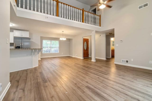 210 Riveredge Way, Mcdonough, GA 30252 - unfurnished living room with a ceiling fan, a chandelier, light wood-style flooring, baseboards, and a high ceiling