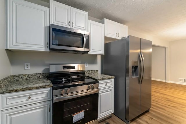 210 Riveredge Way, Mcdonough, GA 30252 - kitchen featuring appliances with stainless steel finishes, light wood-style floors, white cabinetry, a textured ceiling, and baseboards