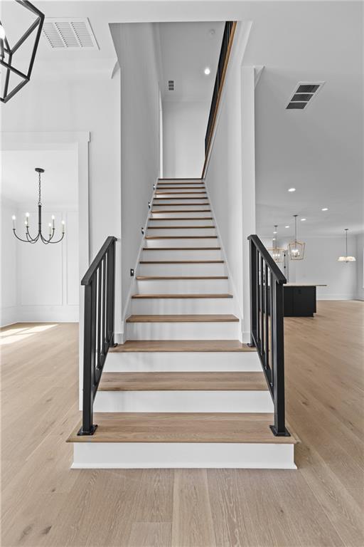 6120 Hutchins Dr, Buford, GA 30518 - stairs with a chandelier, wood finished floors, recessed lighting, and baseboards