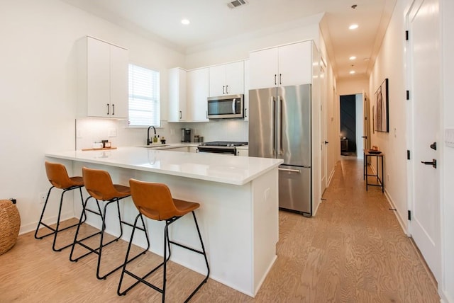 417 E College Ave Unit 102, Decatur, GA 30030 - kitchen with stainless steel appliances, a peninsula, a kitchen bar, light wood-style flooring, and backsplash