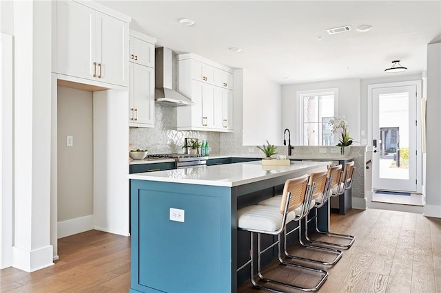 kitchen with wall chimney exhaust hood, light wood-style flooring, a breakfast bar area, decorative backsplash, and a center island