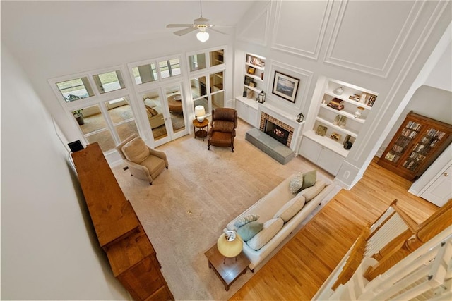 living area with a ceiling fan, a towering ceiling, built in features, a fireplace, and wood finished floors