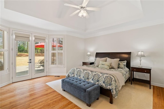 bedroom featuring light wood-style floors, access to exterior, french doors, baseboards, and a tray ceiling