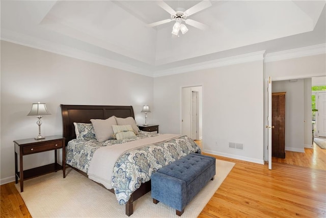 bedroom with visible vents, baseboards, a tray ceiling, a ceiling fan, and light wood finished floors