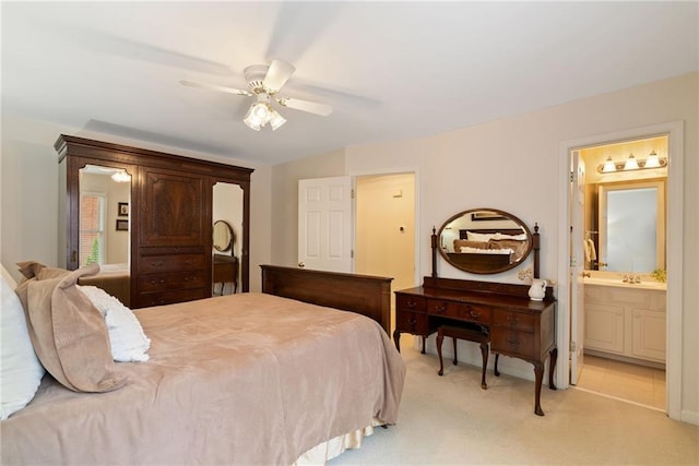 bedroom featuring a sink, a ceiling fan, ensuite bath, and light colored carpet
