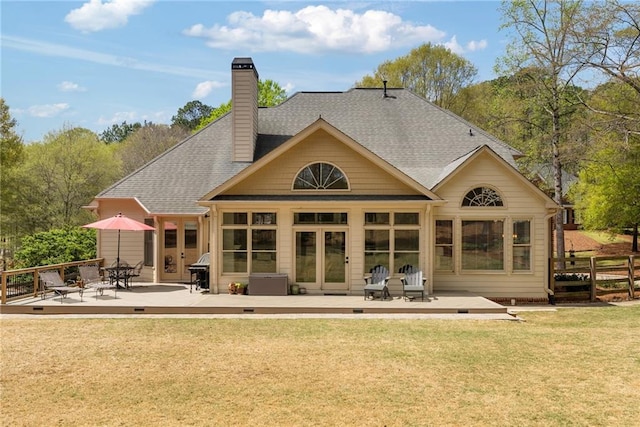 rear view of house with a chimney, french doors, roof with shingles, a deck, and a yard