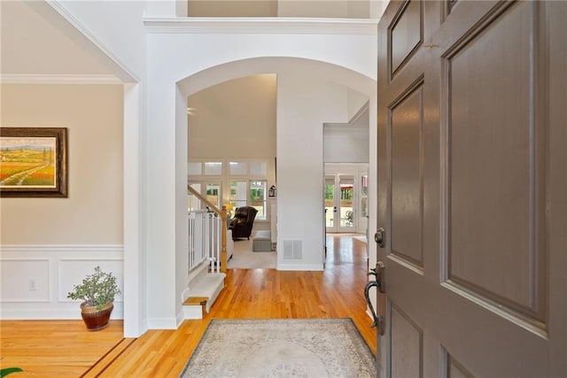 entryway with crown molding, visible vents, stairs, light wood-type flooring, and arched walkways