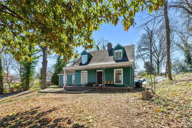 cape cod home with covered porch, a chimney, and cooling unit