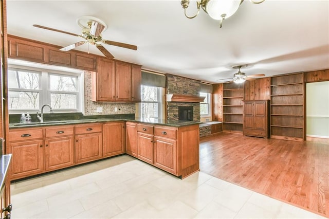 kitchen featuring kitchen peninsula, sink, light wood-type flooring, ceiling fan, and a fireplace