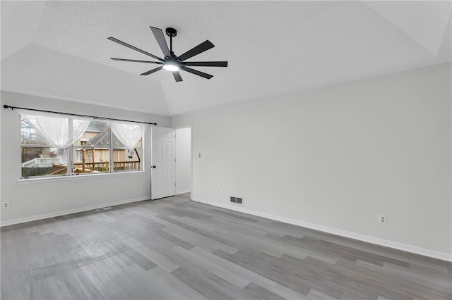 unfurnished room with a textured ceiling, a tray ceiling, vaulted ceiling, ceiling fan, and wood-type flooring